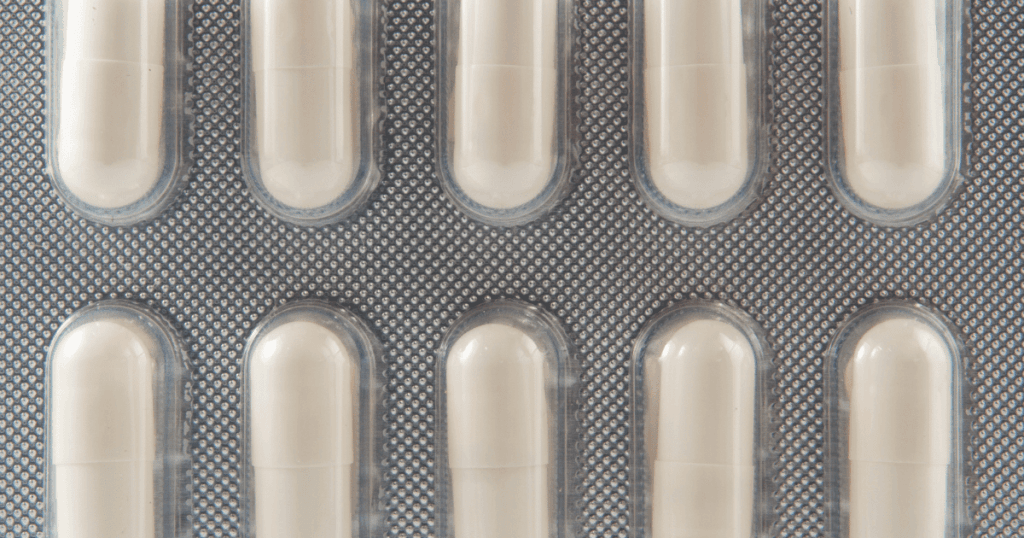 A closeup shot of white filled capsules enclosed in a foil package.